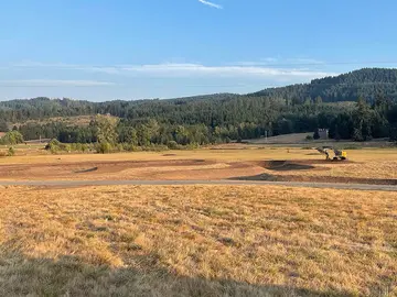 Newly dug pond basin in an open field with an excavator in the background