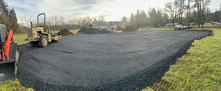 Wide view of the compacted gravel arena base with a roller