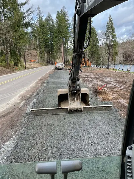 Excavator placing gravel for a pad along the road